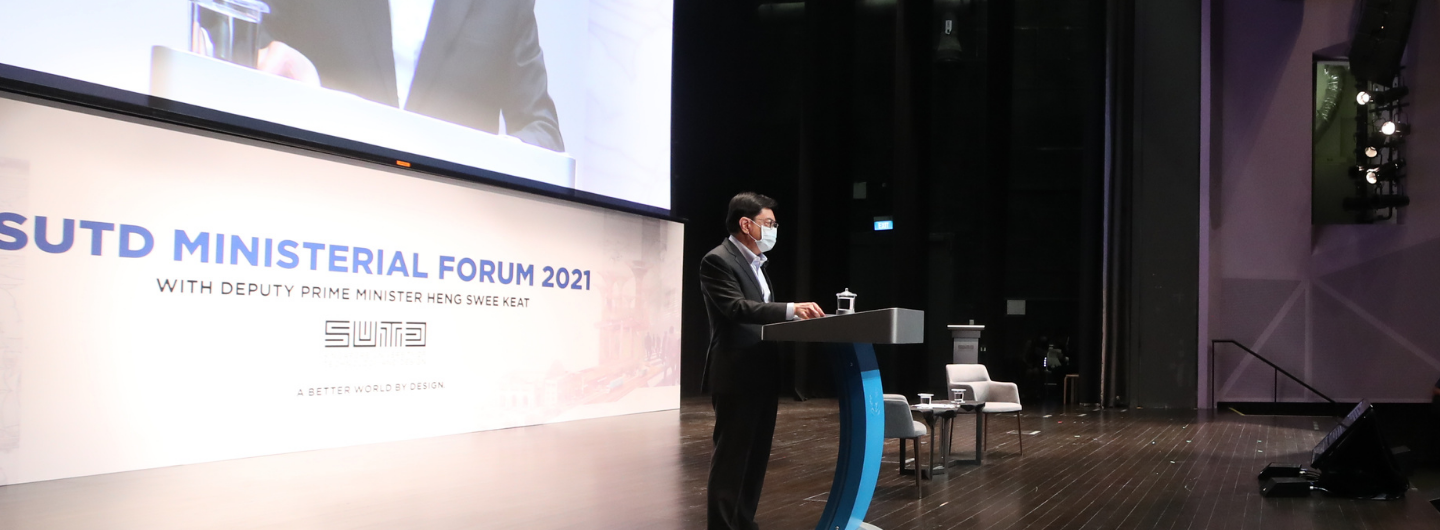Man in mask at SUTD Ministerial Forum 2021 podium, auditorium background.